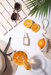 Flat lay of Vitamin c skin care products. Summer props like hat, oranges, palm leaf, goggles in the background. Top view.