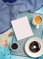 Blank paper on black grid with coffee and donut kept around on blue textured background.