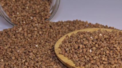Buckwheat in and near a wooden spatula. In the background out of focus transparent jar with buckwheat. Background.
