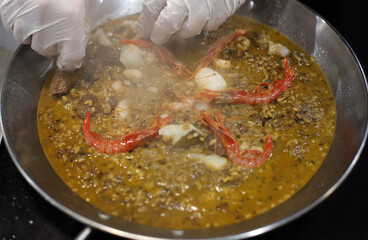 Chef elaborando paella con gambas en paellera con guantes