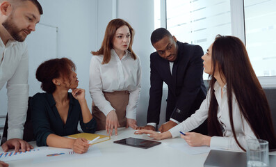 Multiethnic startup team gathering around table and discussing statistics on tablet. Handheld managers brainstorming and planning new strategy. Concept of business