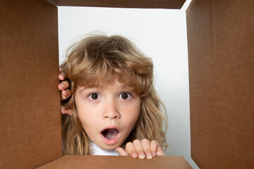 Happy little child boy is opening gift and looking inside cardboard box. Open box and delivery parcel for children.