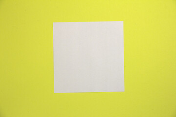 White square sheet of paper. On a yellow background. Top view.
