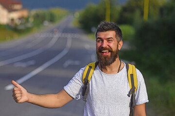 Traveling by autostop, having summer trip. Autostop travel. Man with strict face and beard travelling by hitchhiking with road on background.