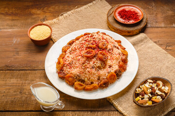 Couscous masfouf with dried fruits in a plate on a wooden table next to saffron, and couscous grits in a bowl and almond milk on a linen napkin.