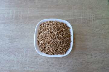 grains of wheat in a white bowl on a wooden kitchen table