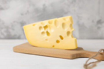 Hard sliced yellow Maasdam cheese on a bamboo board on a light, wooden background. The concept of serving cheese.