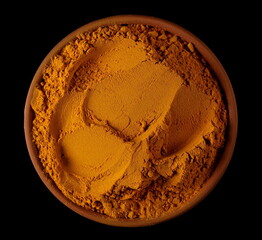 Turmeric (Curcuma) powder pile in clay pot isolated on black, top view