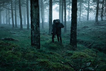 Couple dressed in black and hooded, kissing in a foggy forest. Mysterious movie atmosphere. Kiss and love in the forest.