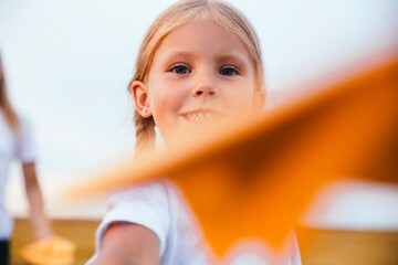 Cute child girl running and playing toy paper airplane in the field in summer day