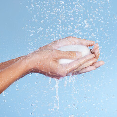 Fototapeta premium Water and soap are your best friends. Studio shot of an unrecognisable woman holding a bar of soap while taking a shower against a blue background.