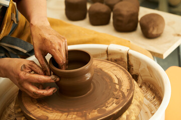 A Potter works with red clay on a Potter's wheel in the workshop..Women's hands create a pot. Girl sculpts in clay pot closeup. Modeling clay close-up. Warm photo atmosphere.