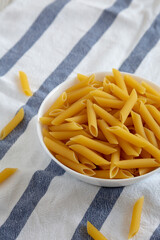 Homemade Raw Dry Penne Pasta in a White Bowl, side view. Copy space.