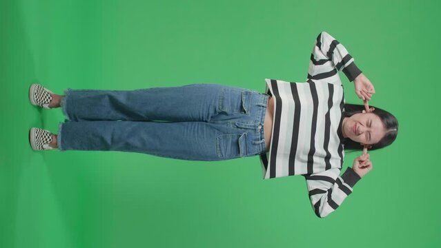Full Body Of Stressed Asian Woman Covering Her Ears While Standing In Front Of Green Screen Background
