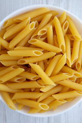 Homemade Raw Dry Penne Pasta in a White Bowl, top view. Flat lay, overhead, from above.