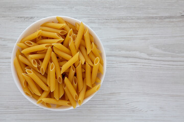 Homemade Raw Dry Penne Pasta in a White Bowl, top view. Flat lay, overhead, from above. Space for text.