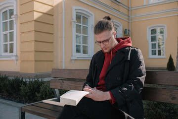 Boy sitting at the bench at the park and writing something