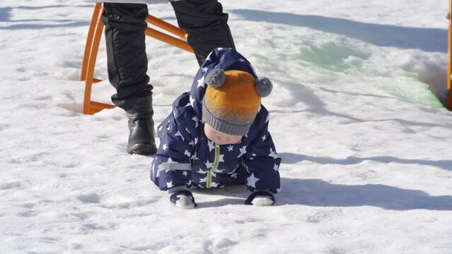Mother with baby on the playground in winter, 1 year old baby boy playing in the snow. High quality 4k footage