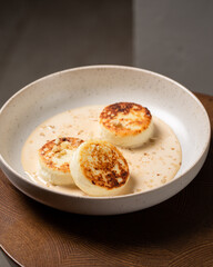 Cottage cheese pancakes or syrniki with caramel sauce and nuts. Concept dark and moody healthy breakfast. Macro and selective focus image.