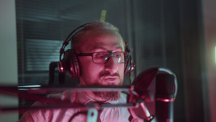 Podcast recording in red lightroom. Middle-aged man in glasses with audio recording