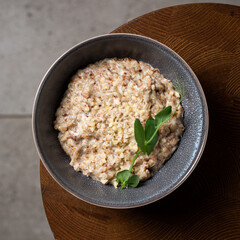 Buckwheat porridge in bowl with cheese on wooden background. Gluten free ancient grain for healthy diet. Top view. Copy space.