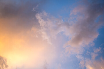 Dramatic sunset landscape with puffy clouds lit by orange setting sun and blue sky.
