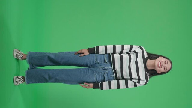 Full Body Of A Smiling Asian Woman Dabbing While Standing In Front Of Green Screen Background  
