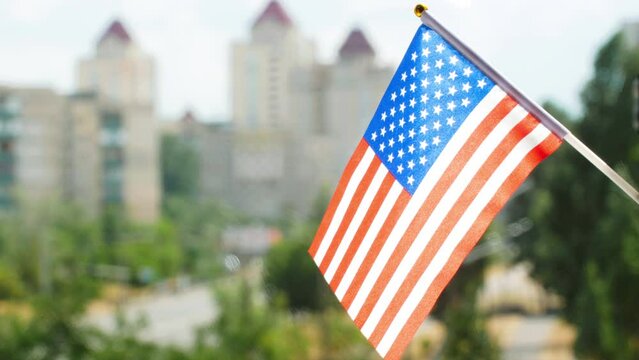 Flag of the United States of America set against blue sky, city street and buildings. Stars and Stripes US flag. American flag waving. The holiday flag of the USA on the sun. Copy space for text