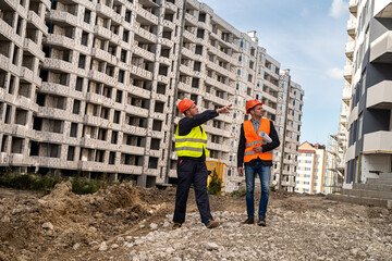 one worker in special clothing shows a hand to the house the other is standing nearby