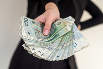  of several banknotes of 100 zlotys of Polish money held in the hands of a woman in a suit.