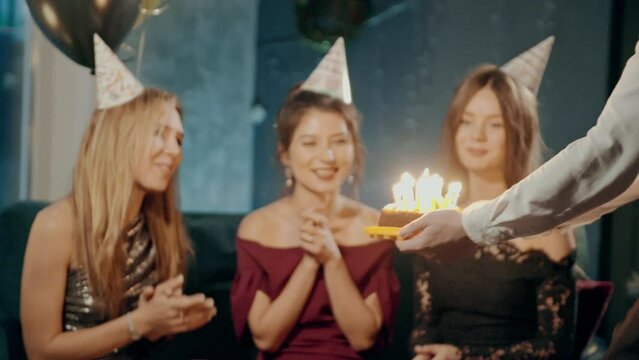 Young woman blowing out fire on candles and making wish at party or celebration. Close-up portrait of smiling asian girl and friends making surprise and taking out birthday cake with candles.