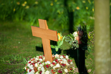 wooden cross and red flowers on a small grave surrounded by grass.