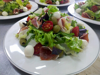 Mediterranean Kitchen. Fresh dietary salad with arugula, mozzarella, prosciutto and cherry tomatoes on a white plate. tasty and healthy food