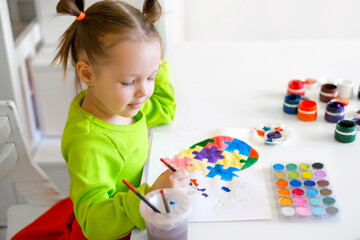 Profile of the cute child sitting at the table. The child paints puzzles forming the shape of a...