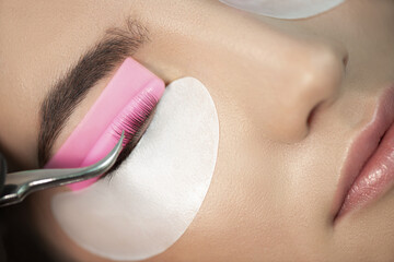 Master glues eyelashes to pink lash roller. Close-up of beauty model's face during lash lift...