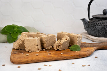 Traditional eastern sweets halva with sunflower seeds and mint leaves on a wooden cutting board. Brewing teapot on the background. Selective focus.