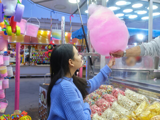 Woman buying a candy cotton from a vendor during a nighttime fair