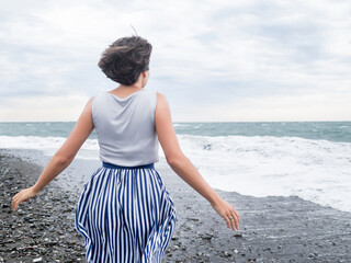 Happy woman greets stormy sea on pebble beach. Woman with hair ruffled with the wind. Wanderlust...