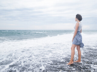 Happy woman greets stormy sea on pebble beach. Woman with hair ruffled with the wind. Wanderlust...