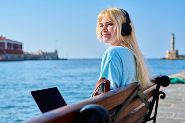 Fototapeta premium Young woman relaxing in headphones with a laptop on the seashore