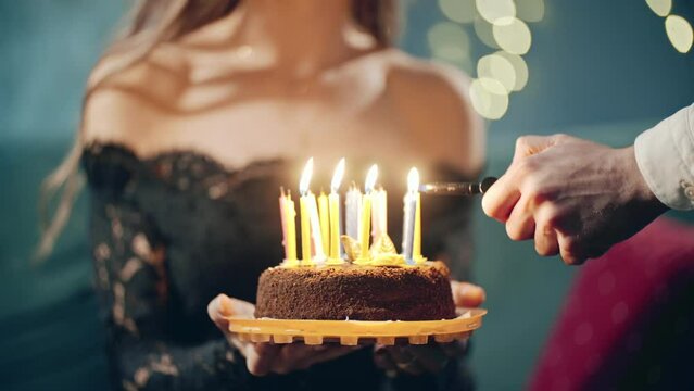 Festive sweet cake with candle which lighting on lighter, burner or fire. Close up of hands holding cake on plate. Surprise for birthday, Party from friends.