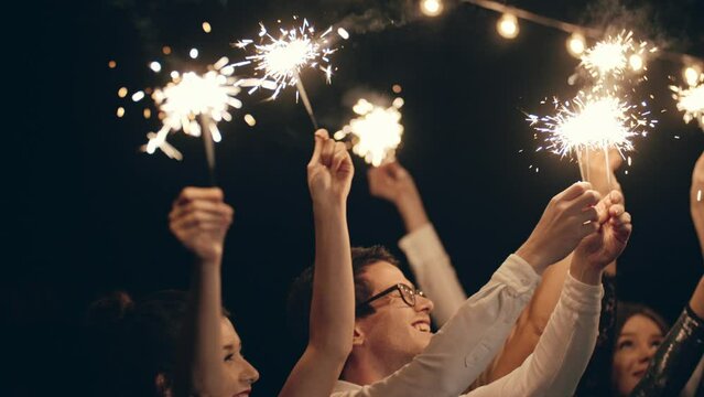 Sparkling lights at birthday party, wedding, Party Party, Party Party, Party. Close-up of hands or palms holding and waving burning sparklers in front of black or dark background.