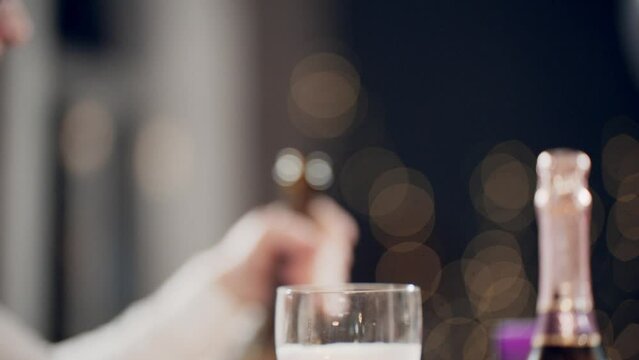 Close-up shot of hands pouring sparkling wine from bottle of champagne into glasses with foam. Multiracial friends celebrating at festive table on Party Party, birthday, Party Party or Party.