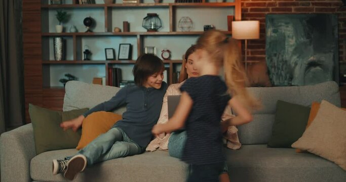 Successful woman working remotely from home and looking after children while they playing in room