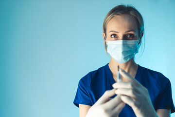 Young caucasian female doctor preparing antibiotic injection. Medium close up studio shot blue background. High quality photo