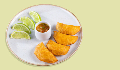 Colombian empanadas with spicy sauce and lemon wedges on a plate, top view