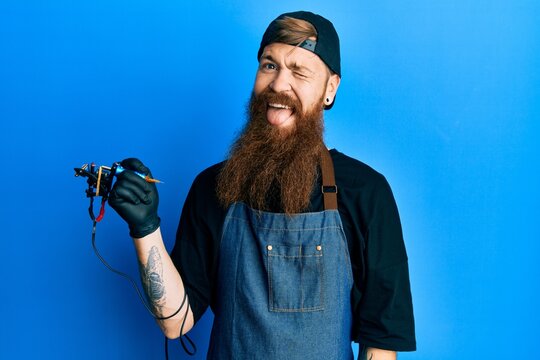 Redhead man with long beard tattoo artist wearing professional uniform and gloves winking looking at the camera with sexy expression, cheerful and happy face.