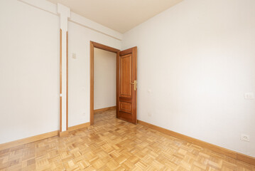 Empty living room with white painted walls, oak parquet floor and dark wooden door