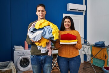 Young couple holding laundry dirty and clean laundry winking looking at the camera with sexy...