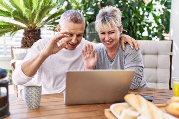 Senior caucasian couple having breakfast and video call using laptop at the terrace.